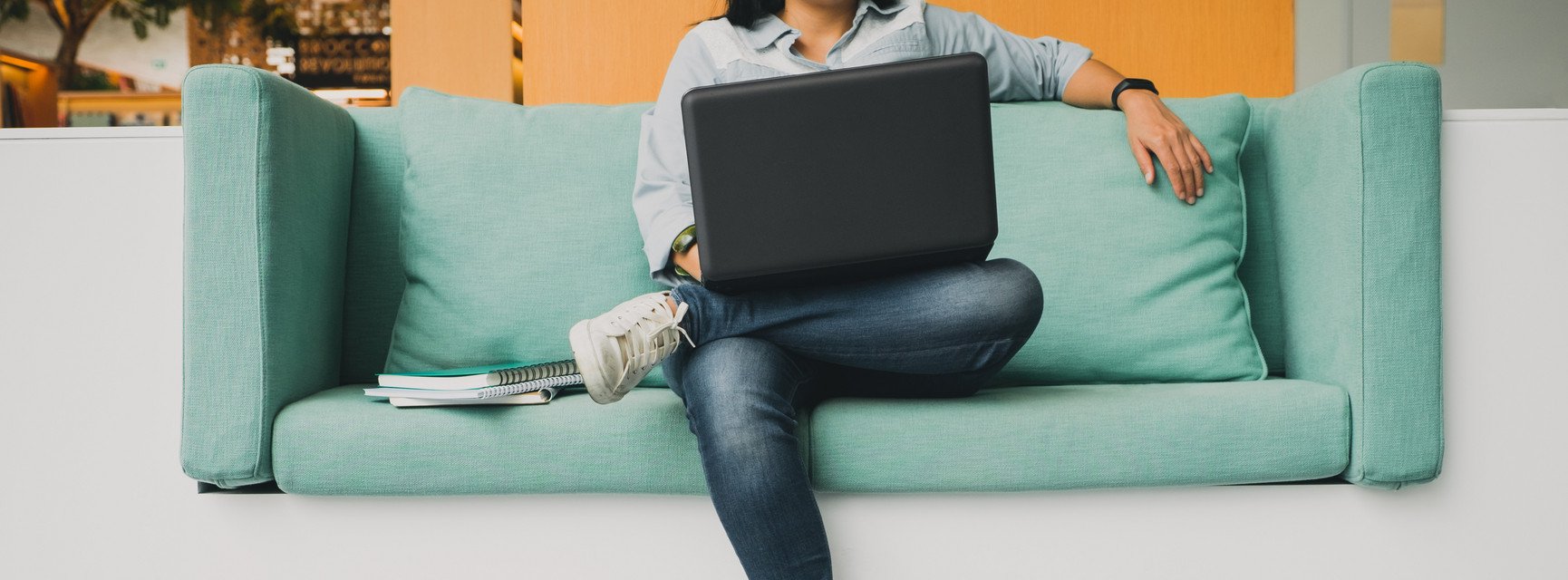 Eine junge Frau sitzt auf dem Sofa und arbeitet an ihrem Laptop.