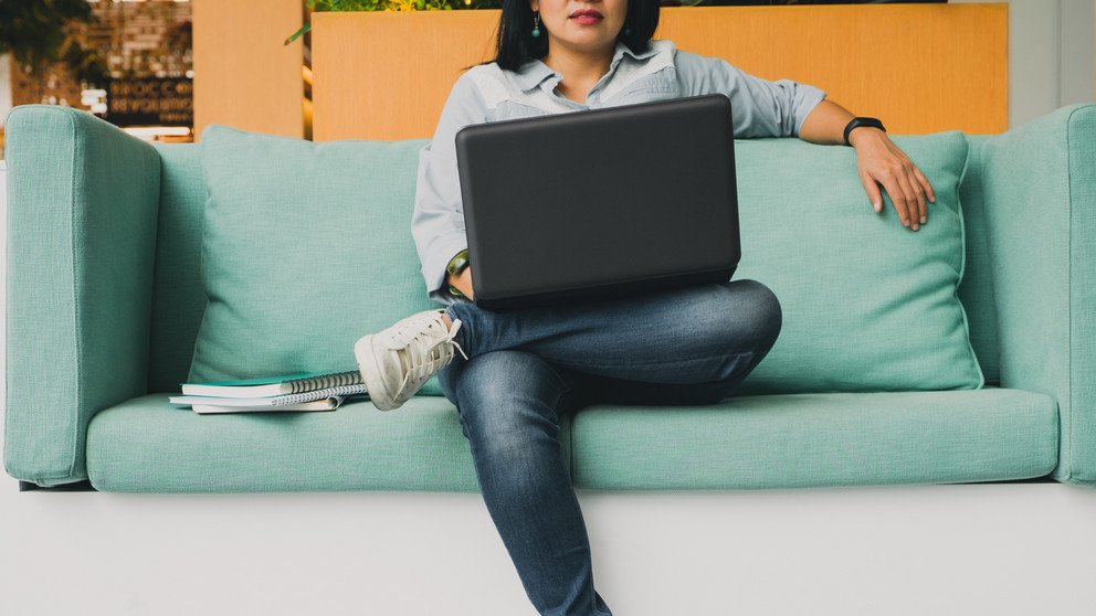 Eine junge Frau sitzt auf dem Sofa und arbeitet an ihrem Laptop.